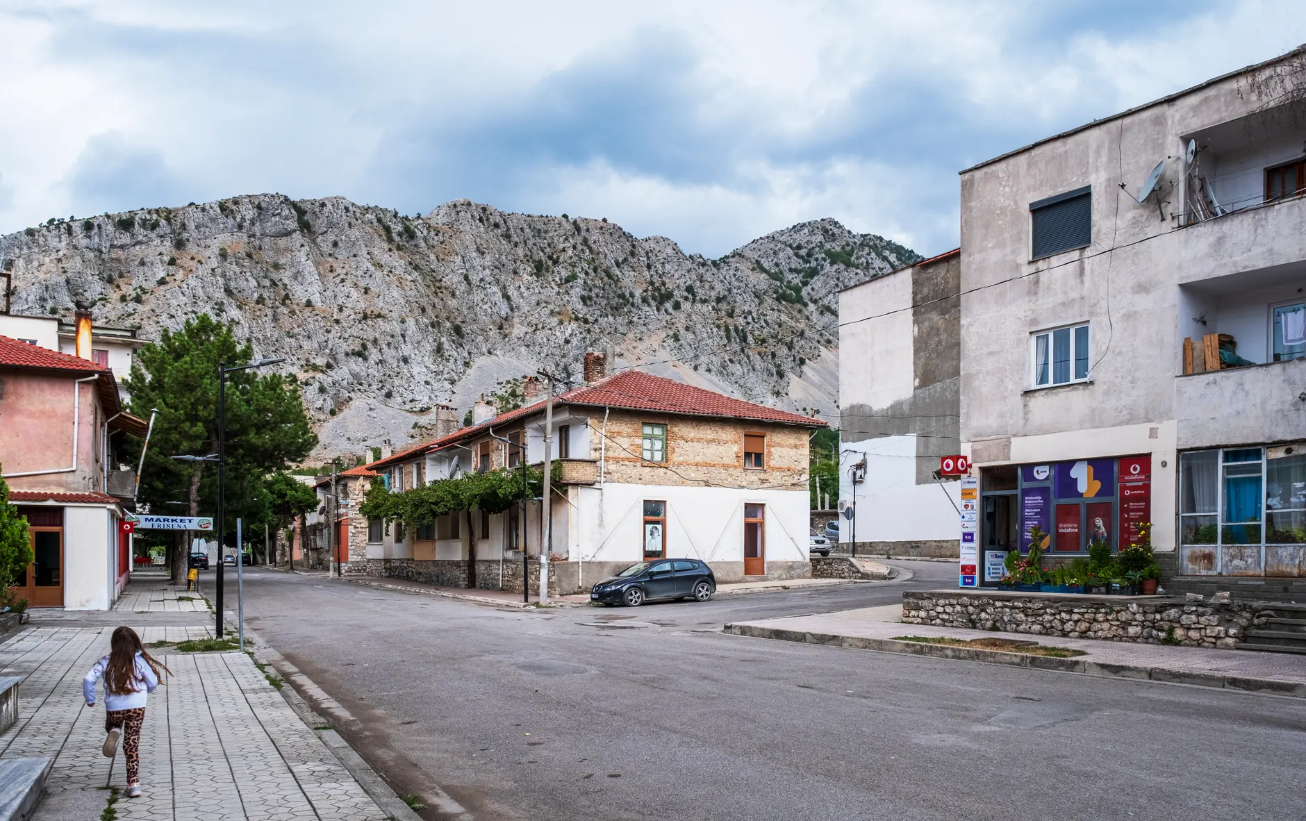 Picturesque village street in Albania with classic architecture framed by rugged mountains.